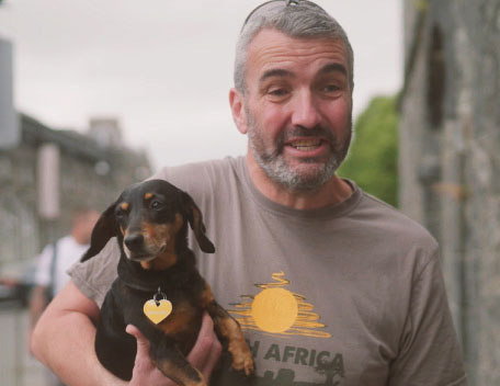 A man in a grey t-shirt holding a small black dog